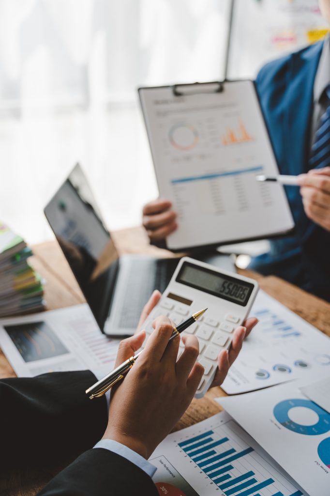 Young colleagues discuss business and analytical price charts using calculators and laptops to calcu